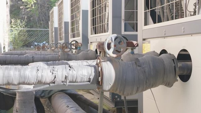 Industrial Pipeline Valve System with Insulated Metal Pipe, Mechanical Fitting, Cooling Equipment, Utility Plant Infrastructure, and Rugged Power Facility Engineering Exterior in Daylight