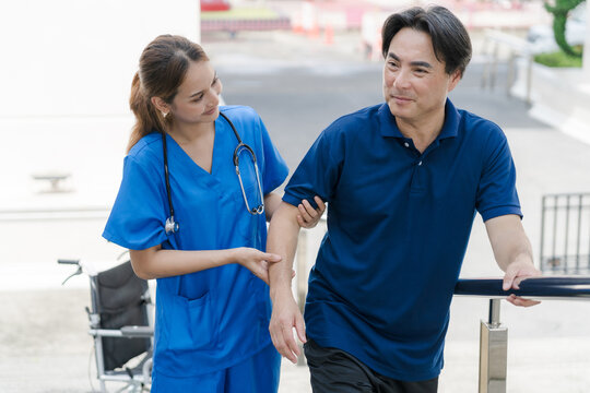 Asian female nurse helping senior male patient to walk for rehabilitation outdoor.