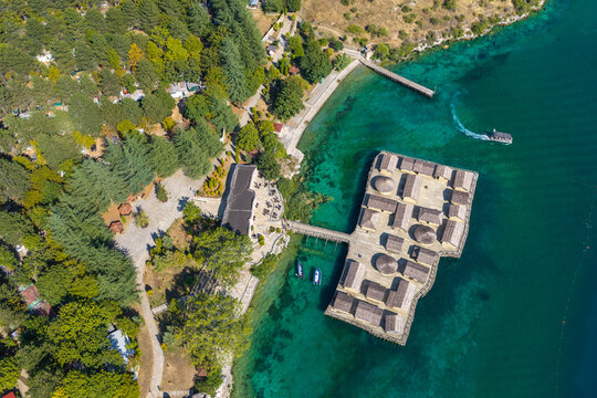 Aerial view of The Bay of Bones Museum with reconstructed wooden pile dwellings, walkways, and boats on the clear turquoise waters of Lake Ohrid in Komuna e Ohrit, North Macedonia.