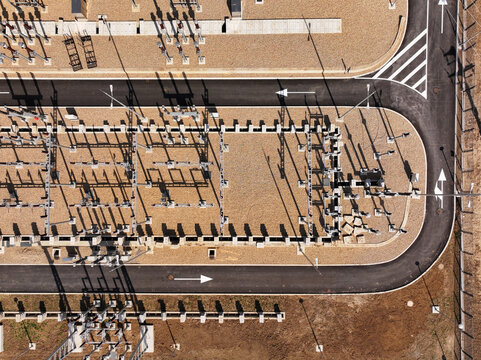 Aerial view of an electrical substation with transformers, power lines, and gravel ground, surrounded by asphalt roads with directional arrows in Serbia.