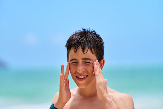 White boy applying sunscreen on beach by ocean on sunny day