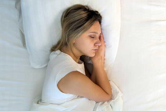 Woman sleeping peacefully on her side with hands tucked under her cheek, top-down view. Restful sleep, serene bedroom, and cozy bed.