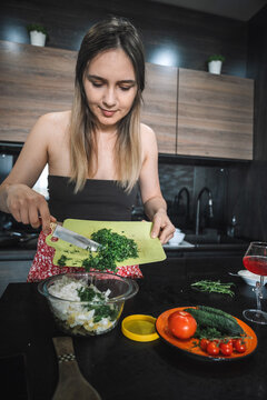 Young attractive woman preparing fresh vegetable salad in a modern home kitchen. Healthy cooking, homemade food preparation, nutrition, and everyday domestic lifestyle.