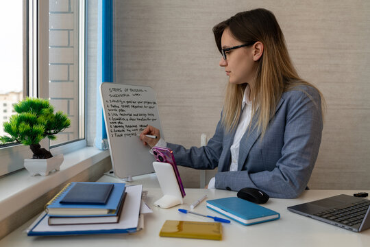 Businesswoman writing a step-by-step work plan on a whiteboard using a marker. Strategic planning, goal setting, and project management.