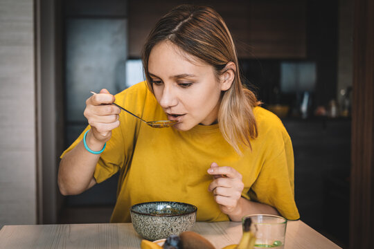 Woman bringing spoonful of food to her mouth during a meal at home. Daily eating routine, healthy diet, and mindful consumption.