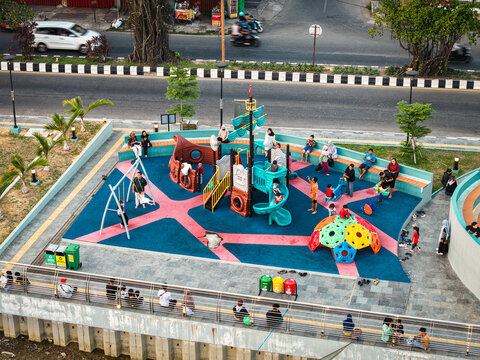 Aerial view of Teras Samarinda 2 playground with colorful play structures, a climbing dome, and swings, with children playing and people sitting on benches in Samarinda, East Kalimantan, Indonesia.