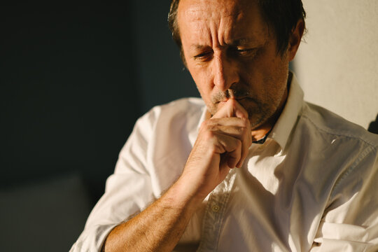 Thoughtful man pausing to reflect outdoors, pensive expression and hand on chin, dramatic shadow and warm light on a sunny balcony.