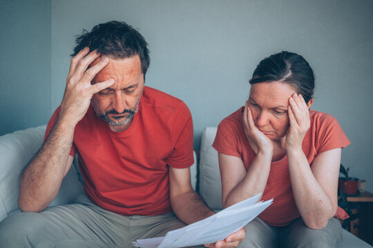 Anxious man and woman sitting on sofa looking at paperwork, facing financial difficulties, expenses and economic uncertainty