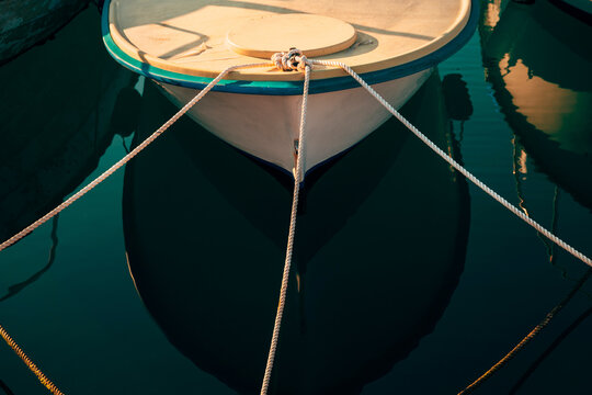 High-angle symmetrical shot of a wooden boat bow tied with mooring ropes in still emerald water.