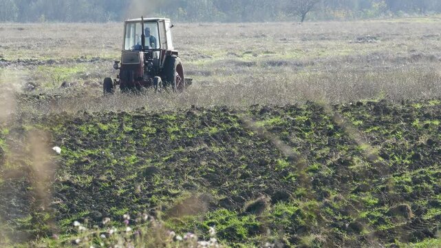 Distant shot of an old Soviet-era vintage tractor maneuvering in a field with an unrecognizable driver, historic Eastern Bloc agriculture machinery working on a farm plantation in Bulgaria