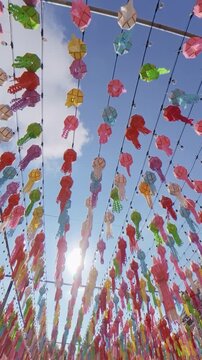 Vertical footage of colorful paper lanterns and decorative tassels hanging from overhead strings against a bright blue sky, creating a festive outdoor atmosphere.