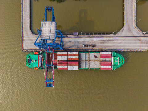 Aerial view of PT Pelabuhan Samudera Palaran showing a container ship docked at the pier with loading cranes, colorful containers, and river water in Samarinda, East Kalimantan, Indonesia.