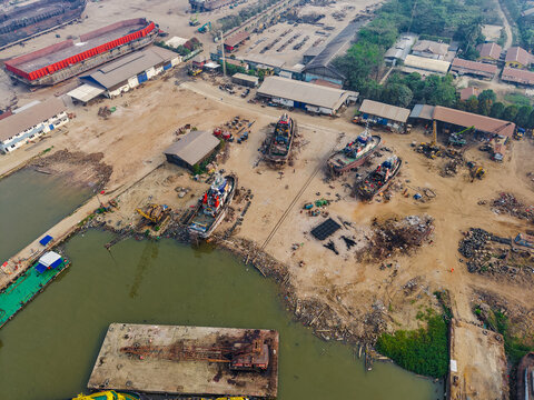 Aerial view of PT. Menumbar Kaltim shipyard with tugboats, vessels under maintenance, warehouses, and heavy machinery along the riverbank in Samarinda, Kalimantan Timur, Indonesia.