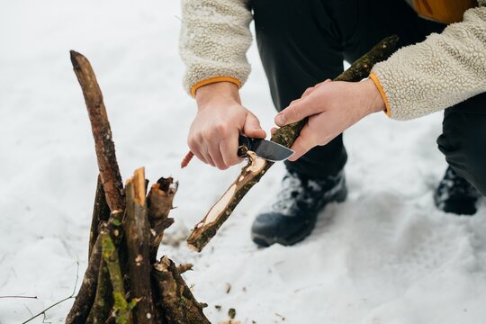 Person preparing wood kindling with knife for winter fire