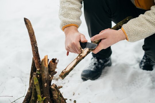 Person preparing campfire kindling with knife in winter
