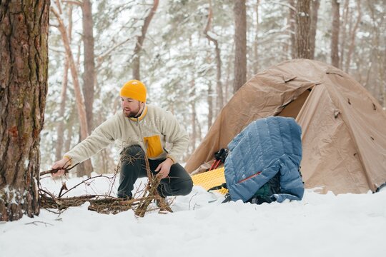Man gathering firewood by winter camping tent