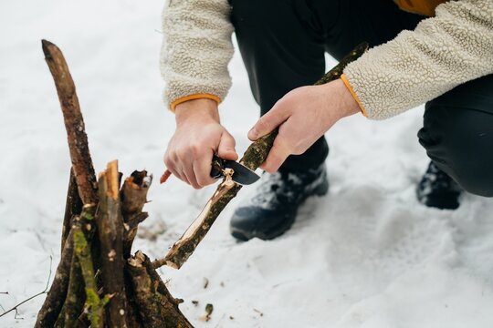 Person preparing kindling with knife for winter campfire