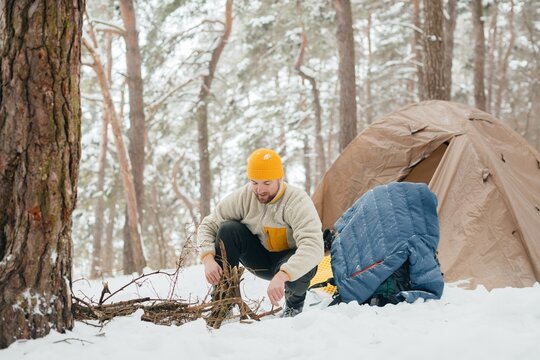Man making campfire in winter forest with tent
