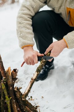 Person preparing kindling with knife for winter campfire