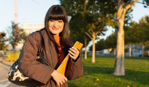 Smiling young student woman holding a folder during the golden hour of autumn