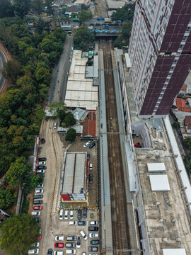 Aerial view of Stasiun Rawa Buntu with railway tracks, a tall apartment building, a parking lot filled with cars, and surrounding greenery in Kecamatan Serpong, Banten, Indonesia.