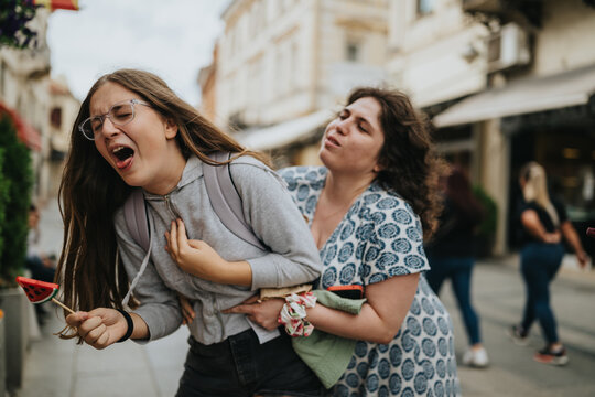 A mother grabs and scolds her teenage daughter as the girl reacts in pain and distress. The heated moment unfolds publicly on a busy urban street with bystanders nearby.