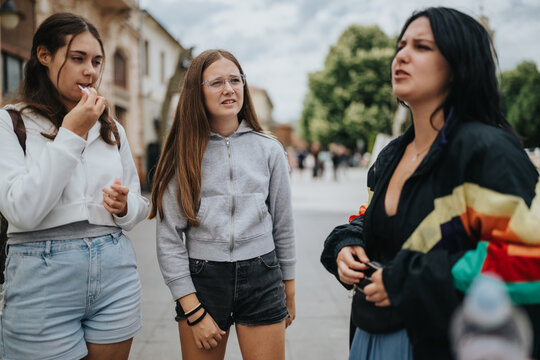 Three teenage girls stand together having a conversation on a pedestrian street. A candid moment of friends talking and listening during a casual urban outing.