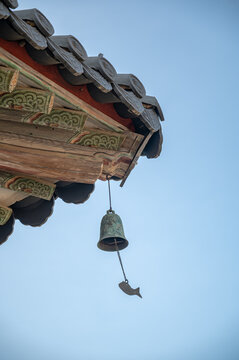 푸른 하늘을 배경으로 법주사 팔상전 목조 처마 밑에서 흔들리는 물고기 풍경.(Wind chime with fish pendant swaying under Beopjusa Palsangjeon wooden eaves against blue sky.)