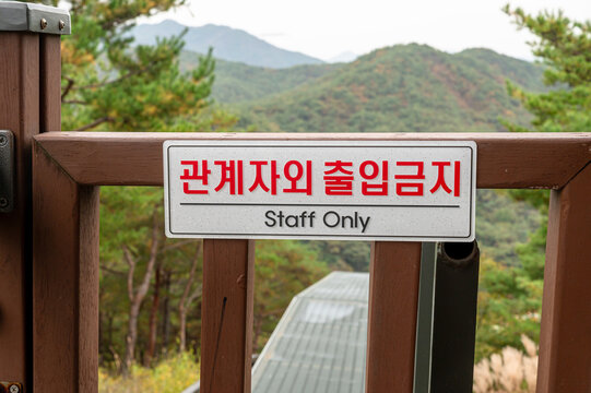 산 배경의 목재 펜스에 한글과 영문으로 부착된 관계자외 출입금지 경고 표지판. (Staff only warning sign in Korean and English on wooden fence with mountain background.)