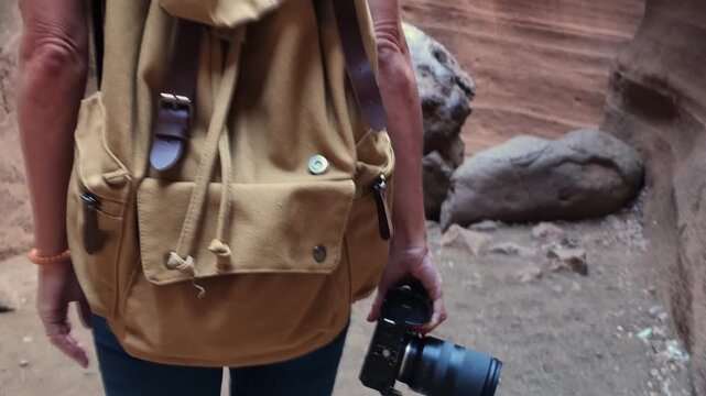 Detail shots of a hiker's hand holding a camera, her canvas backpack and ponytail as she walks between colorful canyon walls in Barranco de las Vacas.
