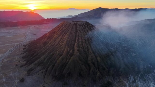 Aerial sunrise view of Gunung Batok extinct volcanic cone, ash slopes, drifting mist, and layered mountain ridges.