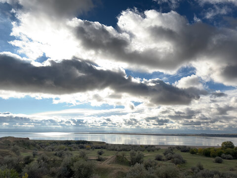 Dramatic cloudy sky with sunlight rain reflecting on calm water. 