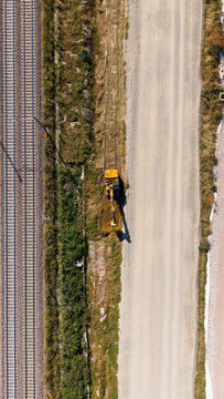 Aerial view of a yellow excavator working on the construction site of a new railway line next to existing tracks in Milan, Lombardy, Italy.