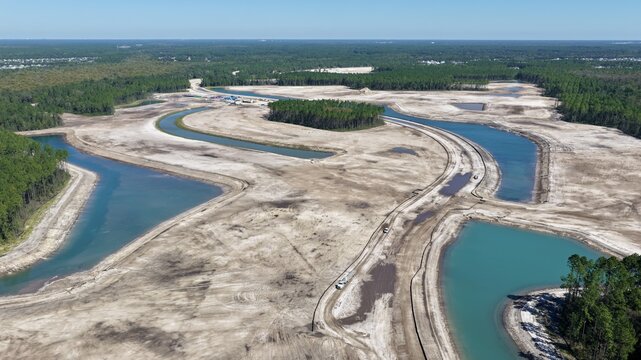Aerial view of a large land development site with winding man-made canals, cleared sandy soil, and surrounding pine forests in St. Johns County, Florida, United States.