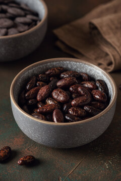 Shelled cacao beans and chocolate buttons in a bowl on a dark rustic background, selective focus, vertical