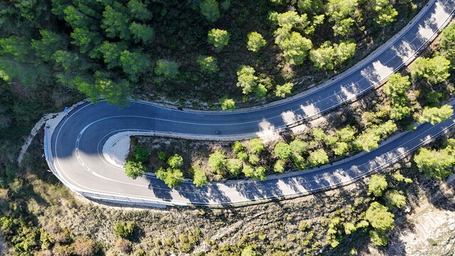 Aerial view of the winding mountain road at Mirador del Coll de Rates de Parcent, surrounded by lush pine forests and rugged terrain in Alicante, Valencian Community, Spain.