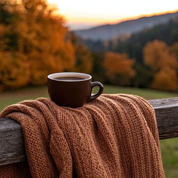 Coffee cup on a woolen throw atop a rustic fence, with golden autumn foliage and distant hills at dusk.