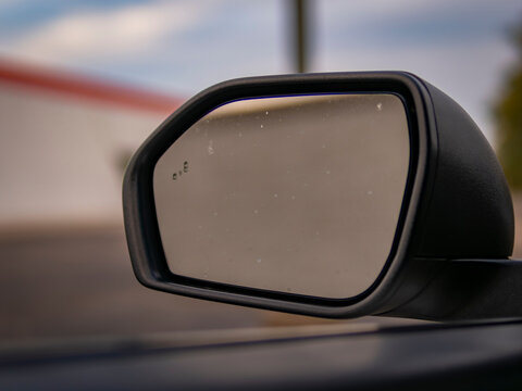 Close up of a vehicle side mirror with raindrops on glass and blind spot monitoring icon