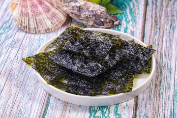 Crispy nori seaweed chips on white ceramic plate with scallop and oyster shells on rustic turquoise wood, snack food © Andrei Starostin
