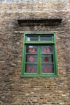 Traditional Green Wooden Window with Red Paper Cutouts on Grey Brick Wall in Jiangnan Residence