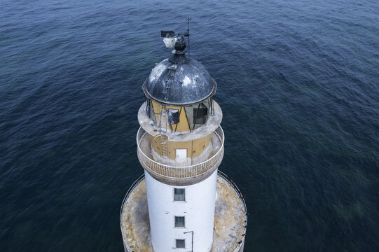 Aerial view of Rattray Head Lighthouse surrounded by the deep blue waters of the North Sea, showing the white tower and lantern room in Peterhead, United Kingdom.