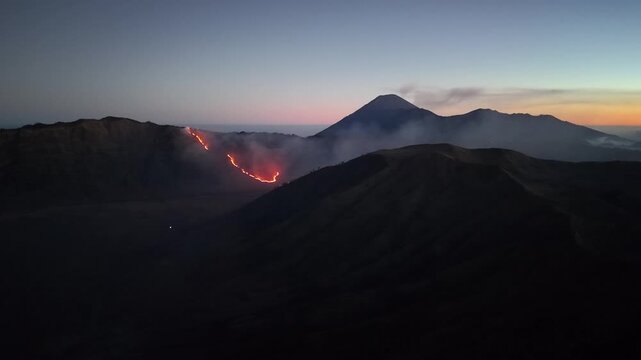 Ground view of fire burning along Mount Bromo caldera rim at sunrise.