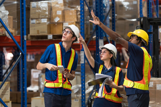 Warehouse workers, warehouse storage and logistics. Professional multiethnic team of warehouse workers discussing logistics plan and checking stock control while working in storage warehouse