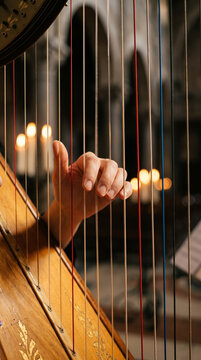 Hands Plucking Strings Of Concert Harp In Candlelit Cathedral