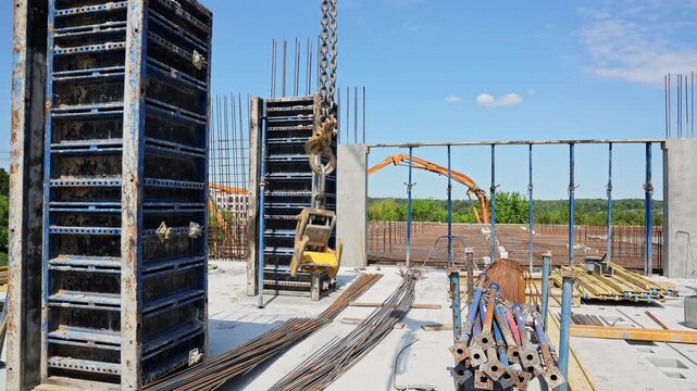 Worker directs a crane hook beside upright wall formwork in direct daylight, Construction crew prepares a tall metal panel for installation outdoors