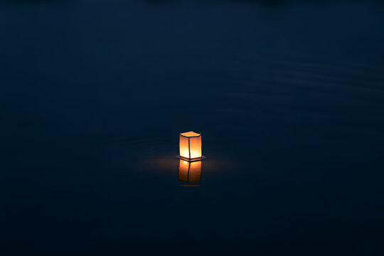 A single glowing paper lantern floats on dark water, casting a warm reflection, creating a peaceful and serene atmosphere at night.