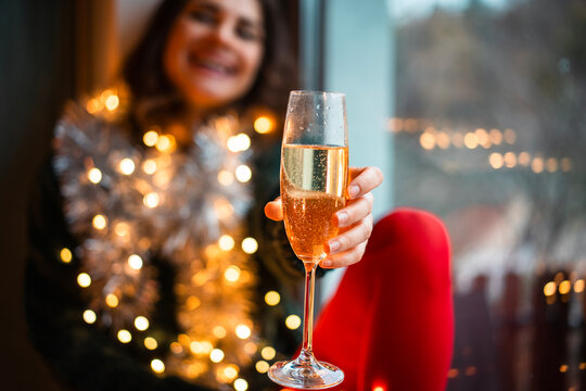 Foreground champagne glass toast with a blurry festive background of a smiling woman.