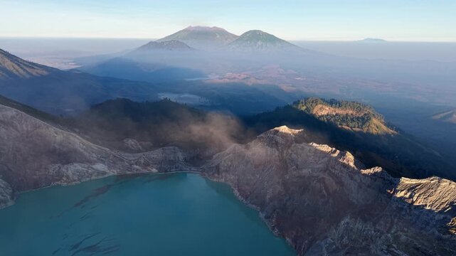 Aerial view of volcanic landscape with turquoise lake. Smoke drifts from crater at Mount Ijen