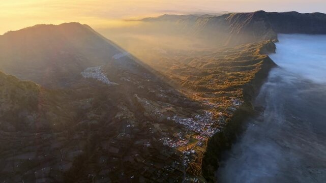 Golden dawn lights valleys with mist rising gently. Mountains loom large. Fog curls around cliffs at Bromo