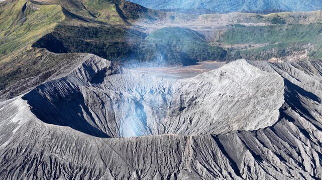 Volcano spews smoke from its crater. Rugged slopes surround the smoking peak at Bromo